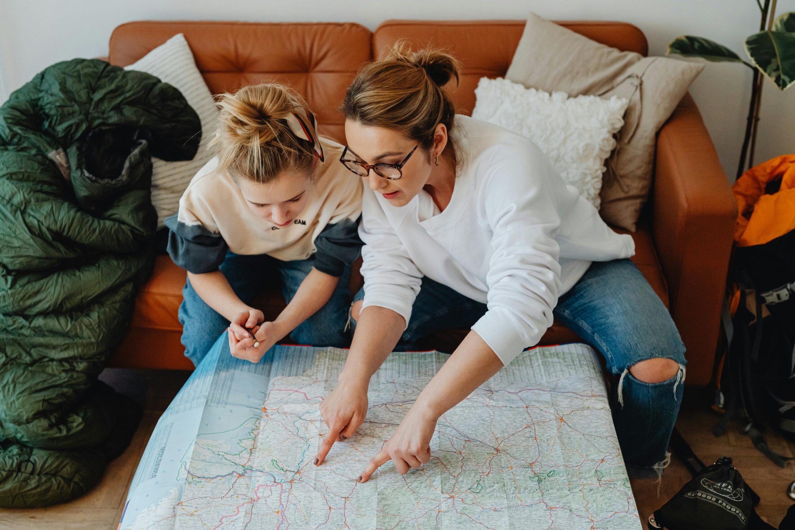 A mother and daughter discussing travel plans using a large paper map on the sofa.